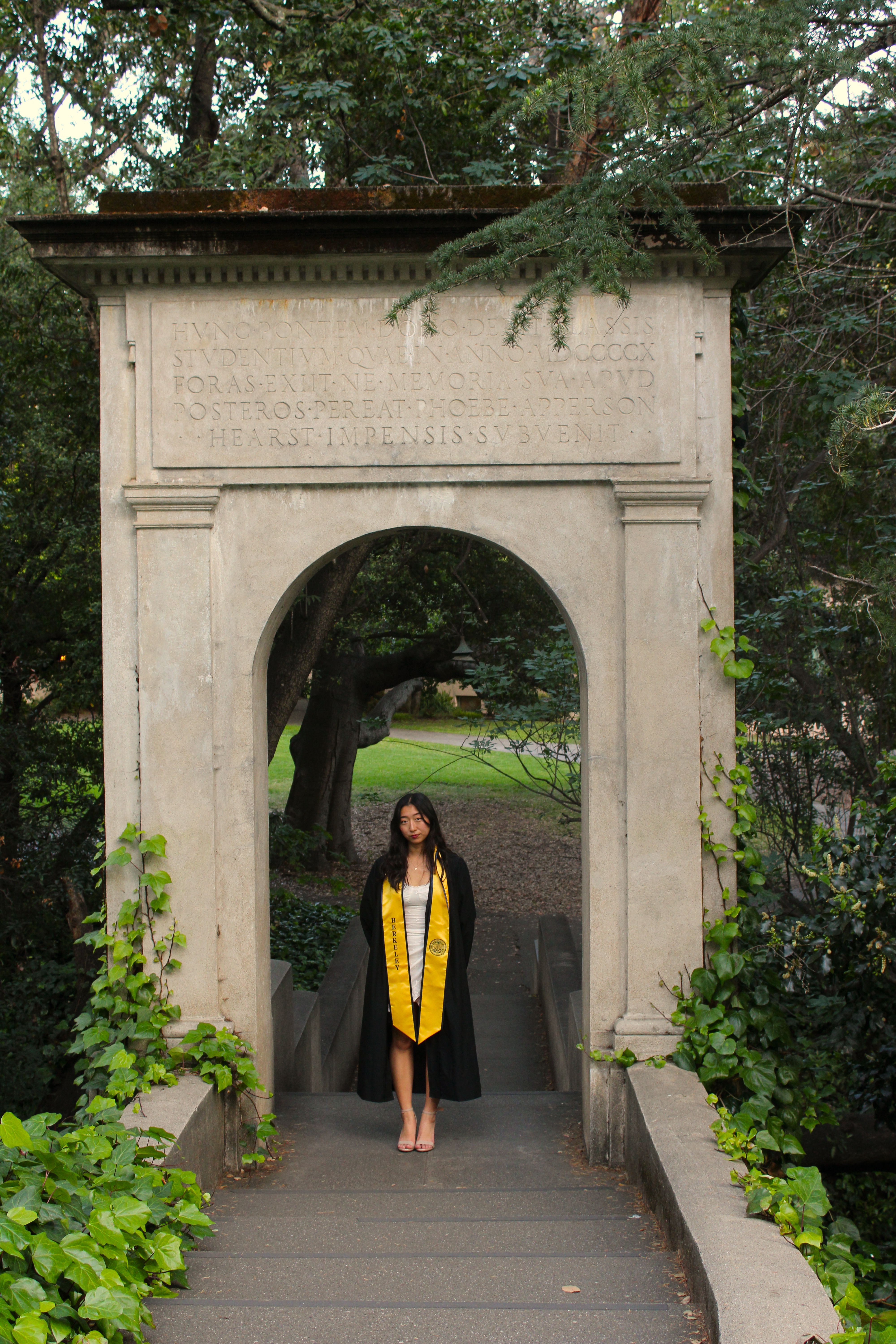 The author, Allyson, standing in a cap and gown, under an archway at UC Berkeley.